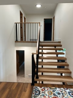 Hickory open treads on black stringers with black balusters and handrail rising to a balcony landing.