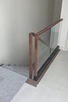 Frameless base rail glass with a walnut cap and squared walnut newel at the head of a stair