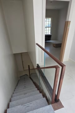 Frameless base rail glass with a walnut cap and squared walnut newel at the head of a stair