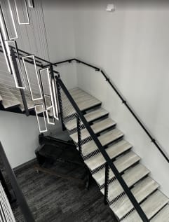 Light gray treads on a black steel stair with cable railing and wall handrail beneath hanging LED pendants.