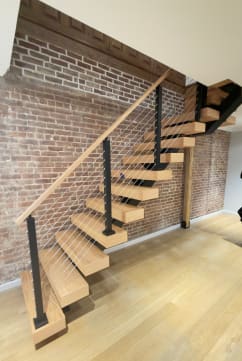 White oak floating stair on a black mono stringer with cable railing against an exposed brick wall