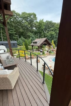 Black cable railing sweeps along a curved composite deck above a landscaped pool yard.