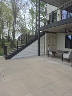 Dark composite stair with cable railing climbs from a covered patio to an upper deck among trees.