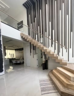 Light oak cantilevered treads rise from stacked plinth steps along a wall of black vertical slats in a glossy white foyer.