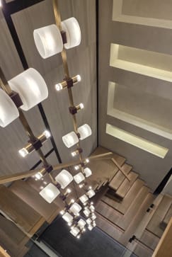 Looking down a stairwell past a column of pendant lights to floating oak treads and glass railing