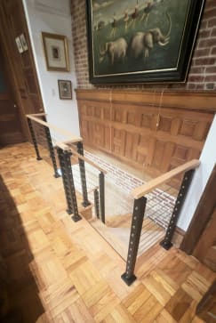 Black-post cable railing with a white oak cap wraps a stair opening on parquet floors in a historic townhouse