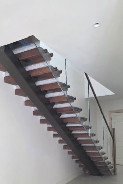 Walnut floating treads on a dark stringer with standoff-pin glass and walnut handrail in a bright stairwell