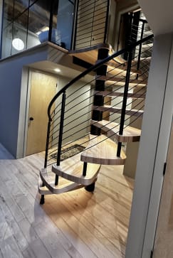 A curved floating spiral stair with light wood treads and black rod railing in an industrial loft.