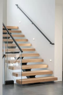 White oak floating treads on a hidden mono stringer with glass railing and a black wall handrail with wall returns.