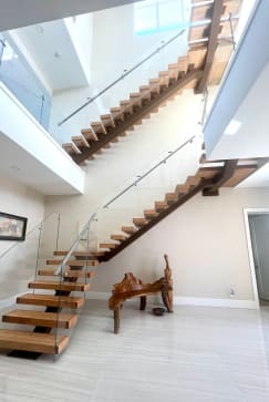 Looking up a wood mono-stringer floating stair with glass railing and a glass-railed loft above.