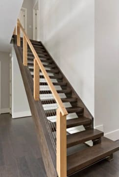 Dark wood open-riser stair with natural wood posts, handrail and cable infill against a white wall.