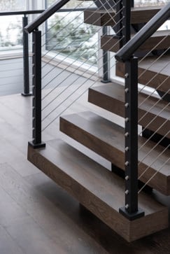 Thick stained oak treads with black cable posts and handrail at the base of a floating stair.