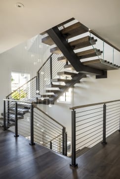 A black FLIGHT Mono climbs through several levels with dark oak treads, glass and horizontal cable railing under glass pendants.
