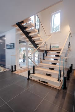 Light oak treads on black mono stringers with glass between black posts at a switchback landing.