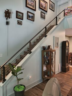 Bronze cable railing tops a white knee wall along a long stair beneath framed art.