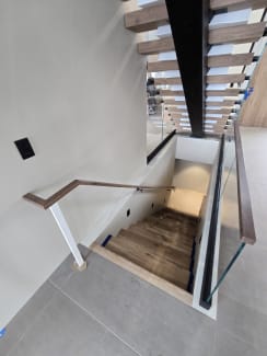 Looking down a stairwell lined with base rail glass and a walnut handrail, with a floating stair rising overhead