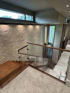 Glass railing with wood handrail at the top landing of a walnut stair beside a stone wall