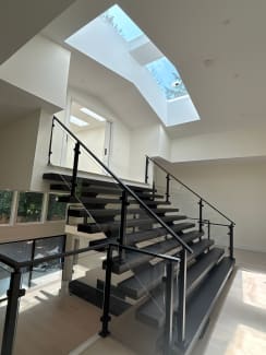 Dark floating stair with post-to-post glass railing beneath a skylit vaulted ceiling