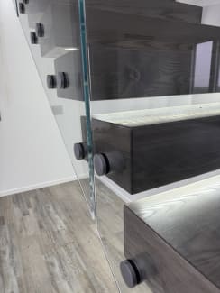 Detail of frameless glass on round standoff pins attached to dark cantilever treads with LED lighting