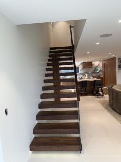 Walnut cantilever stair with glass railing and LED-lit base rising toward a kitchen