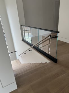 Base rail glass with a black top cap and a wall-mounted handrail connecting to the glass at a stair opening