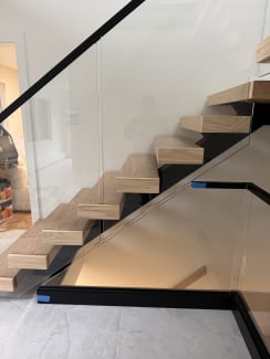 Side view of white oak floating treads beside frameless glass and a black base rail
