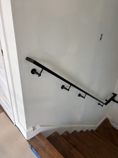 Black steel wall-mounted handrail descending a dark-tread stair