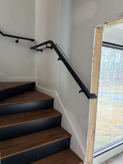 Black steel wall handrail follows a turning stair with walnut treads and black risers