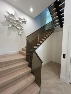 White oak floating stair with smoked glass railing and a black top cap beside a white sculptural wall piece