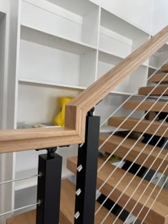 Red oak handrail mitered over black cable railing posts beside floating treads