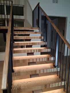 Looking up oak floating treads glowing with LED lighting between black modern baluster railings and oak handrails.