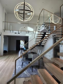 Light oak FLIGHT Mono treads and frameless standoff-pin glass railing climb beneath a sculptural ring chandelier.