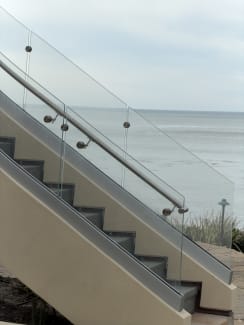 Frameless glass on stainless standoff pins with a stainless handrail lines an exterior stair overlooking the ocean.
