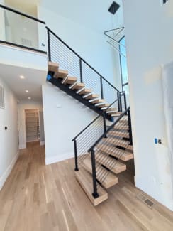 White oak floating treads on a black mono stringer switchback with black cable railing in a bright modern home.