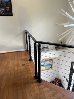 Black-post cable railing turns a corner at an upstairs landing with oak floors.
