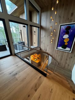 A frameless glass guard set in a black base channel wraps the stair opening beneath tall windows and a pendant chandelier.