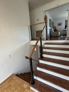 Black cable railing posts with a warm wood handrail line a split-level stair with white risers and cherry-toned treads.