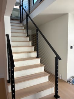 Black posts and handrails with stainless cables flank a straight white-riser oak stair.