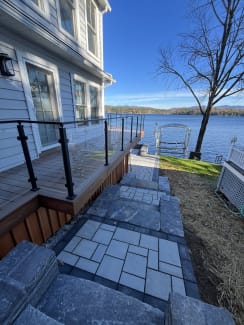 Black posts hold glass panels along an ipe deck overlooking a lake with autumn trees.
