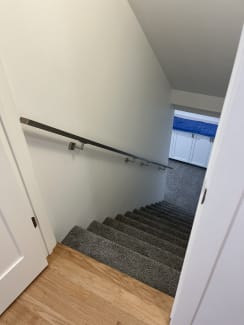 A brushed stainless wall-mounted handrail runs down a carpeted stair in a white stairwell.