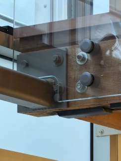 Close view of round standoff pins fastening a glass railing panel to a steel-plated timber beam.