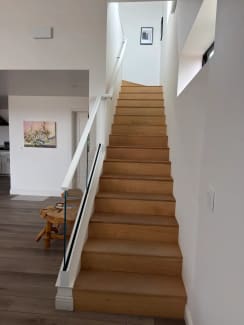 A long oak stair rises along a white wall with a frameless glass guard and slim white handrail.