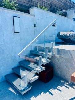 Frameless glass railing on stainless spigots follows exterior stone steps beside a plaster wall.