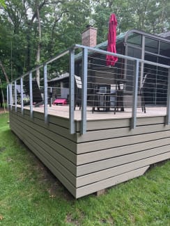 Silver posts and stainless cable infill surround a tan composite deck with patio furniture.