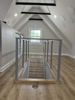 Silver cable railing guards a stair opening in a bright attic bonus room with wood floors.