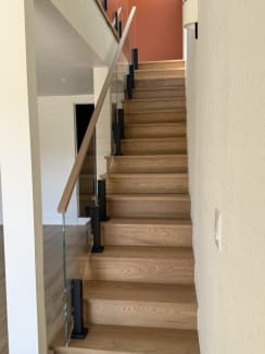 Frameless glass on black Ascend Talons with a white oak handrail lines a closed white oak stair.