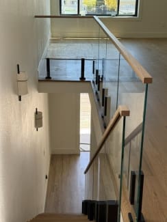 Looking down a stairwell lined with glass on black talons and white oak handrails.