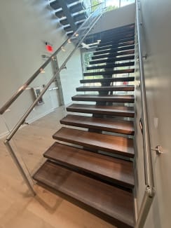 Dark-stained FLIGHT Mono treads with integrated Vedera glass and stainless handrails in a commercial stairwell.
