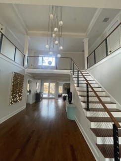 Cable railing with dark wood handrail lines a straight staircase and upper balconies in a bright entry hall.
