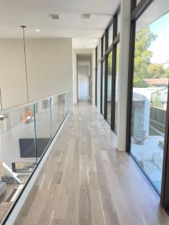 Frameless glass railing in a white base rail lines an upper hallway beside floor-to-ceiling windows.